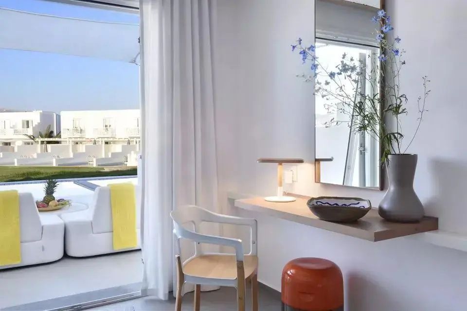 Schreibtischbereich in einem Zimmer mit Spiegel, Stuhl und Blick auf den Außenbereich.