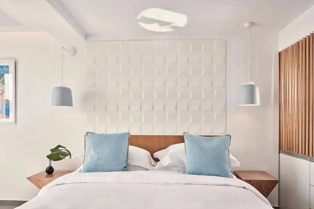 Weißes Doppelbett mit zwei hellblauen Kissen vor einer strukturierten Wand.
