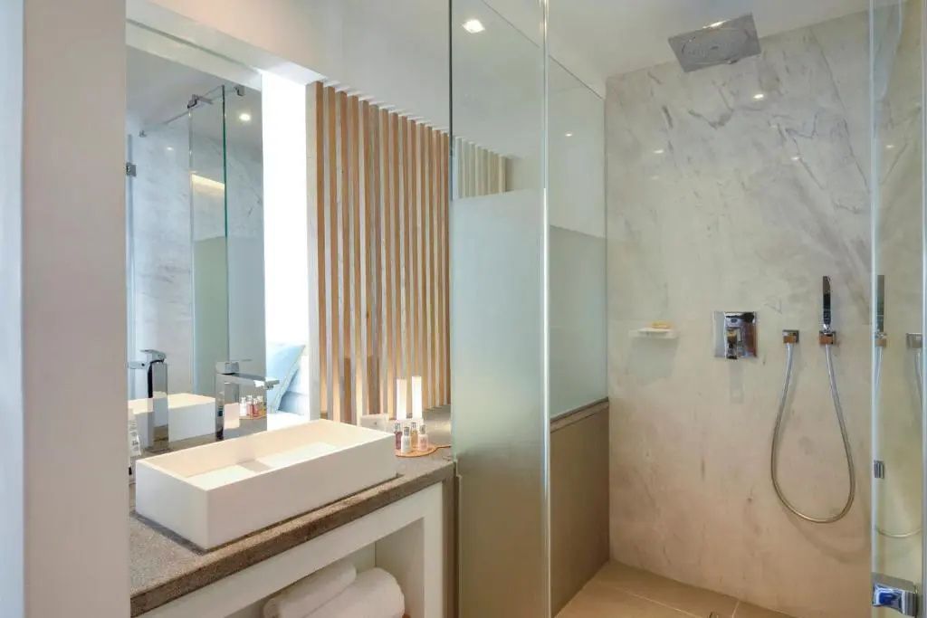 Modernes Badezimmer mit weißem Aufsatzwaschbecken, Regendusche und Glastrennwand.
