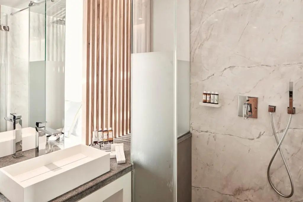 Modernes Badezimmer mit eckigem Waschtisch, gläserner Duschwand und Pflegeprodukten.