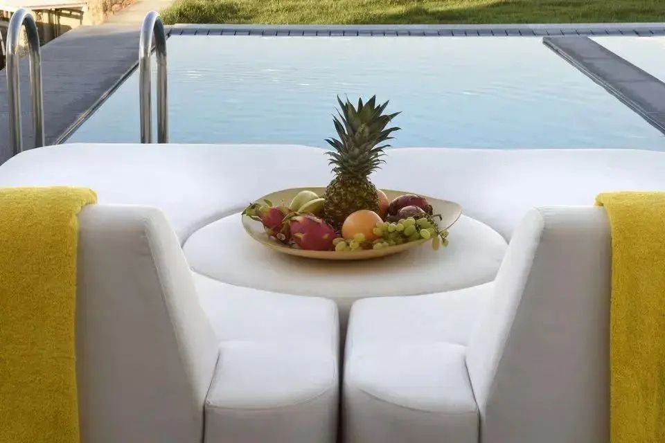Weiße Lounge-Sitzmöbel direkt am Pool mit einer frischen Obstschale im Vordergrund