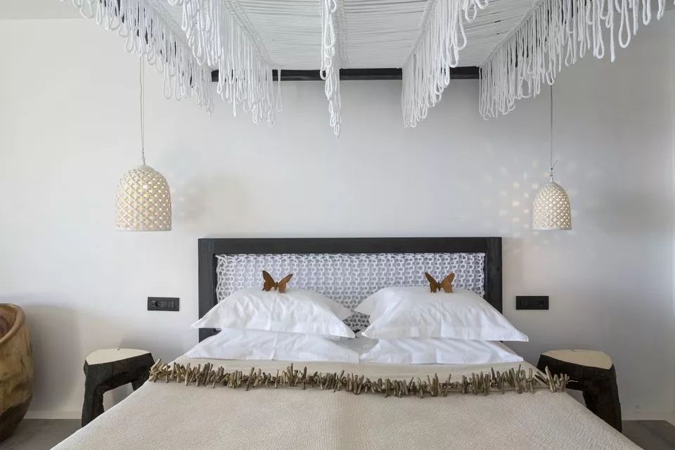 Doppelbett mit weißen Kissen, Schmetterlingsdeko und Lampenschirmen.