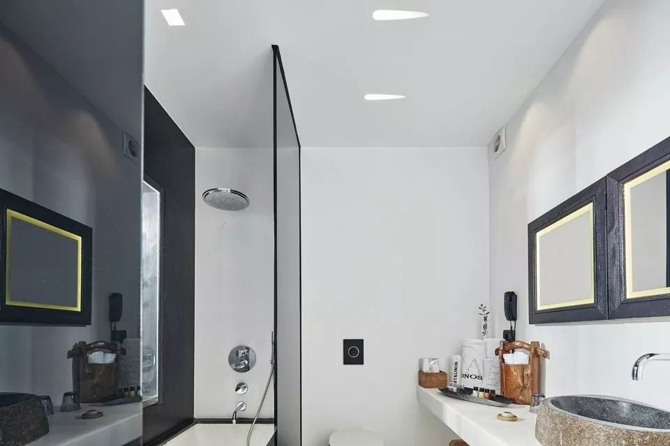 Badezimmer mit Dusche hinter einer Glaswand, weißem Waschtisch und dunkler Wand.