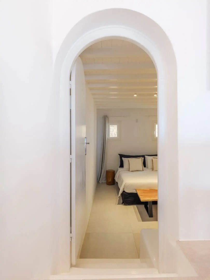 Blick durch einen weißen Rundbogen auf ein Schlafzimmer mit Doppelbett und Holzdecke.