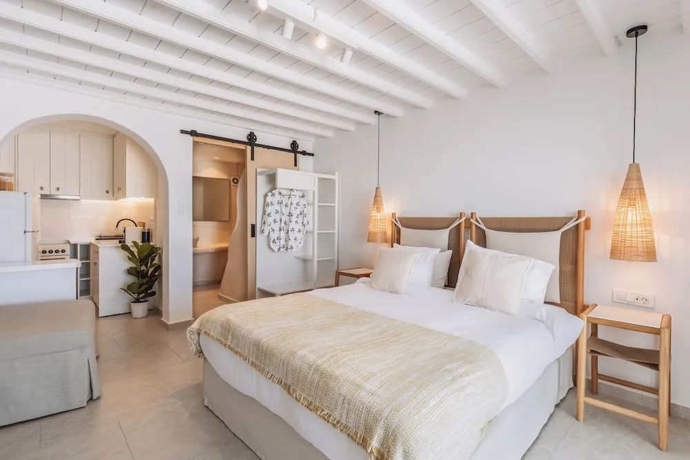 Helles Schlafzimmer mit Doppelbett, Balkendecke und Zugang zum offenen Schrankbereich.