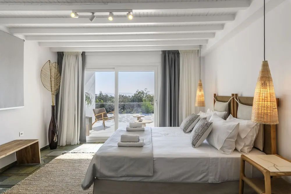 Heller Schlafraum mit weißem Doppelbett, Balkontür und Terrasse dahinter.
