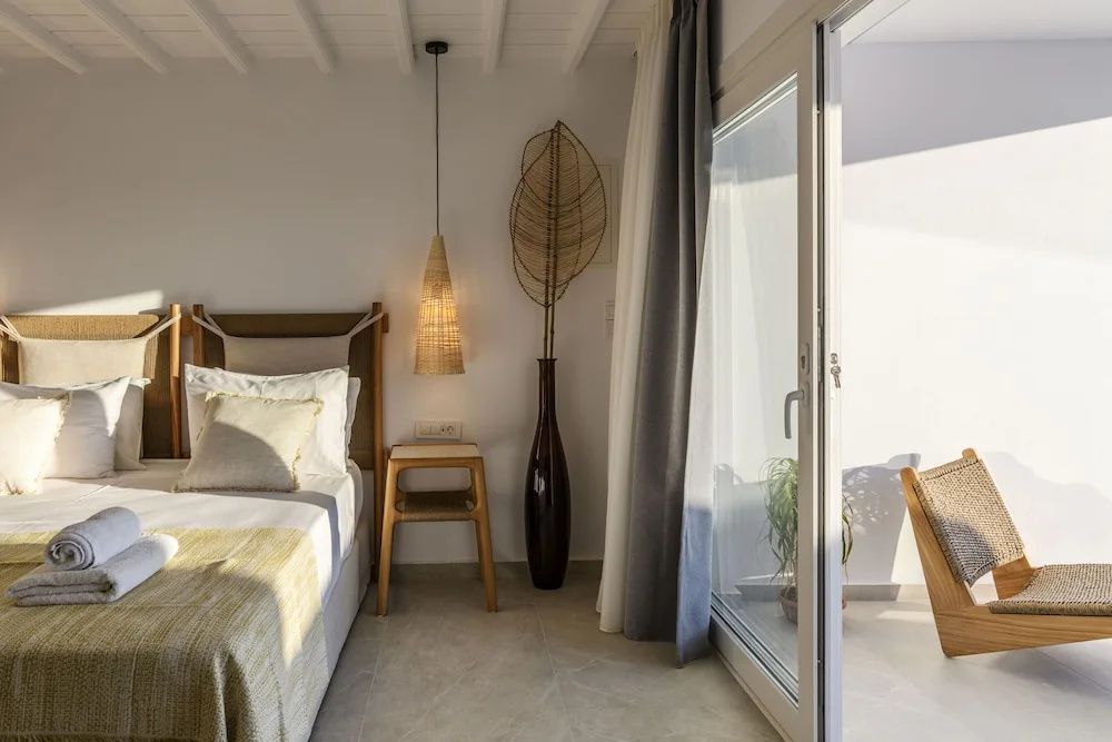 Zimmer mit Bett, Nachttisch aus Holz und hoher Glasschiebetür zur Terrasse.