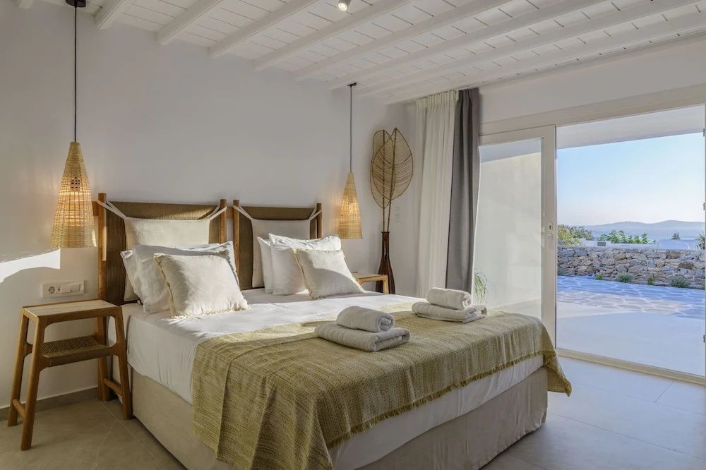 Helles Schlafzimmer mit Doppelbett, beigefarbener Decke und Zugang zur Terrasse.