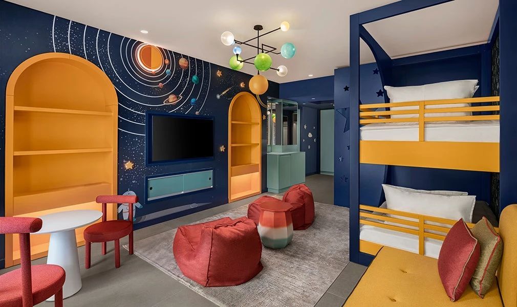 Buntes Kinderzimmer mit Weltraum-Tapete, Etagenbett und roten Sitzsäcken.