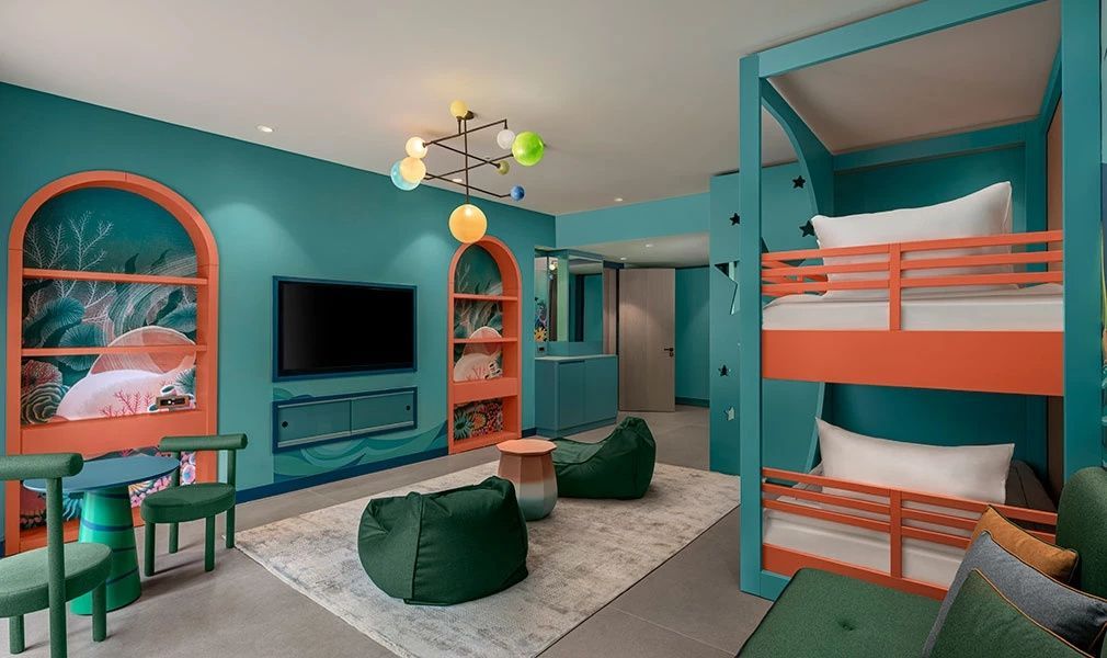 Ein bunt eingerichtetes Kinderzimmer in Blautönen mit Etagenbett und Fernseher.