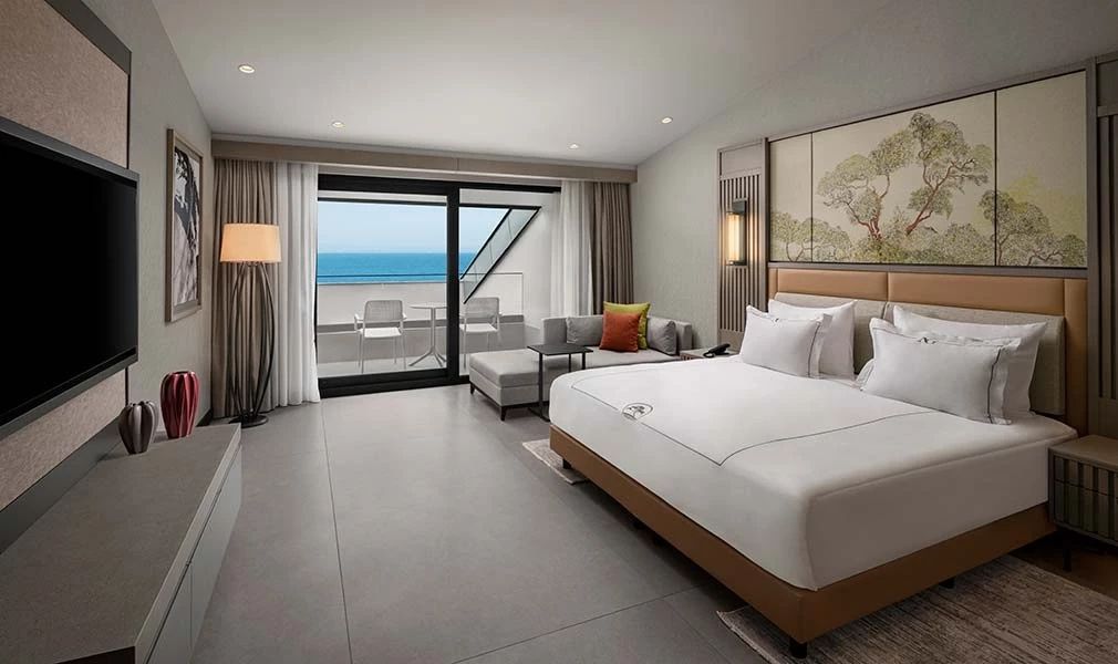 Modernes Doppelzimmer mit Couchecke und Zugang zum Balkon mit Blick auf das Meer.