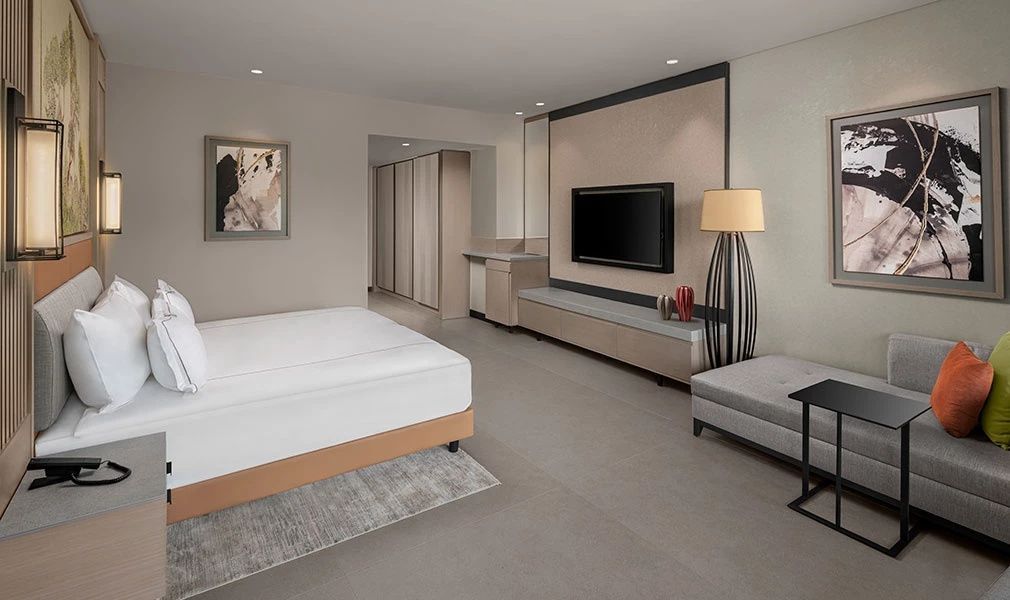 Schlafbereich im Hotelzimmer mit Wandfernseher und moderner Stehlampe.