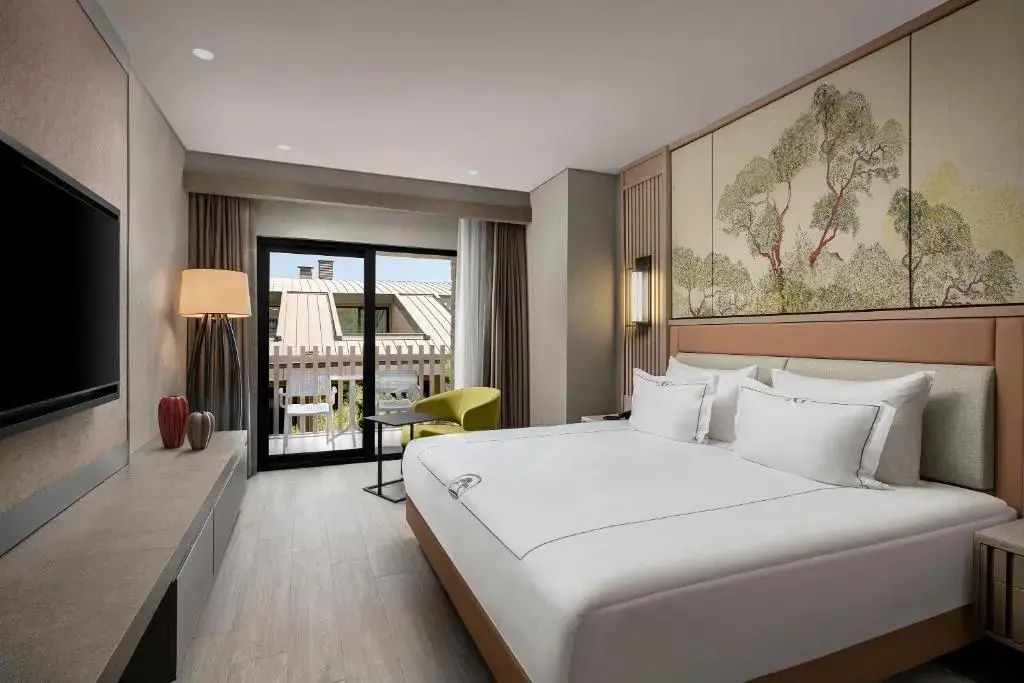 Hotelzimmer mit Doppelbett, gelbem Sessel und Balkon mit Blick auf die Anlage.