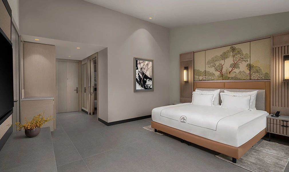 Schlafbereich im Hotelzimmer mit großem Bett, Wandbild und Flurtür im Hintergrund.