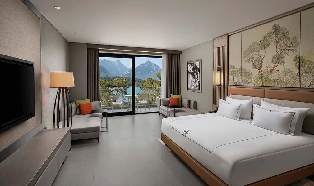 Schlafzimmer mit großem Doppelbett, Sitzbereich und Balkonaussicht auf Berge und Meer.