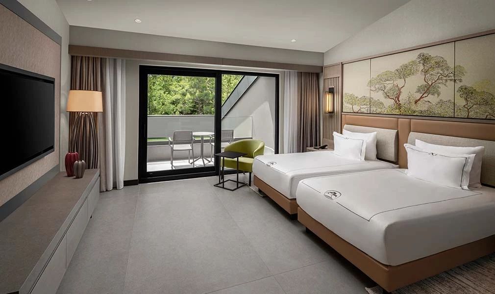 Modernes Hotelzimmer mit zwei Betten, grüner Sitzgelegenheit und Zugang zum Balkon.