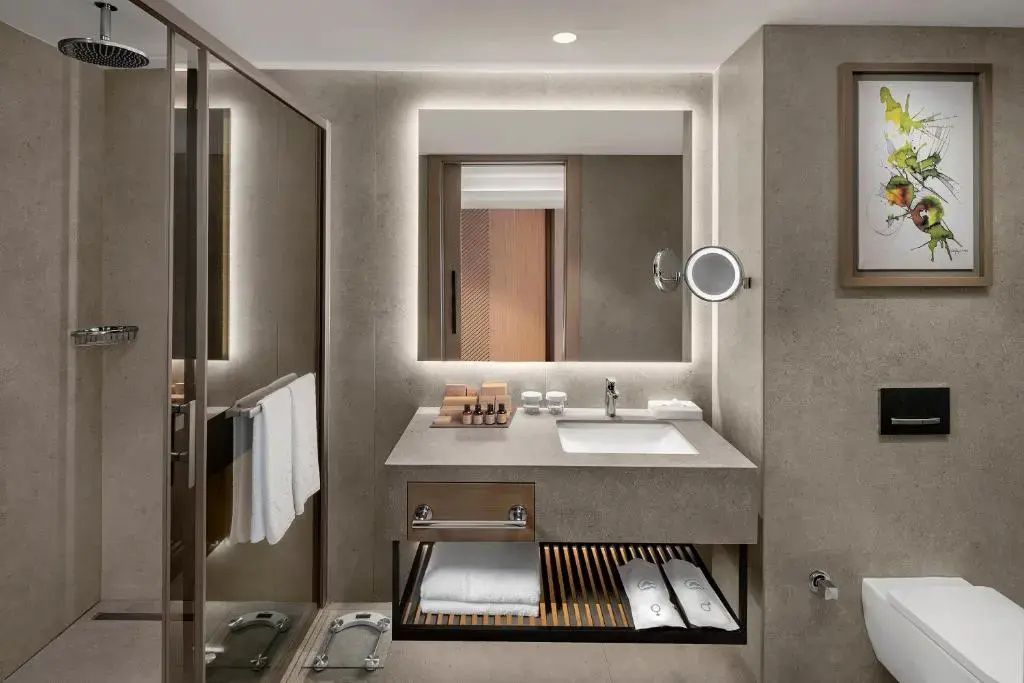 Modernes Badezimmer mit beleuchtetem Spiegel, Waschtisch, Pflegeprodukten und Dusche.