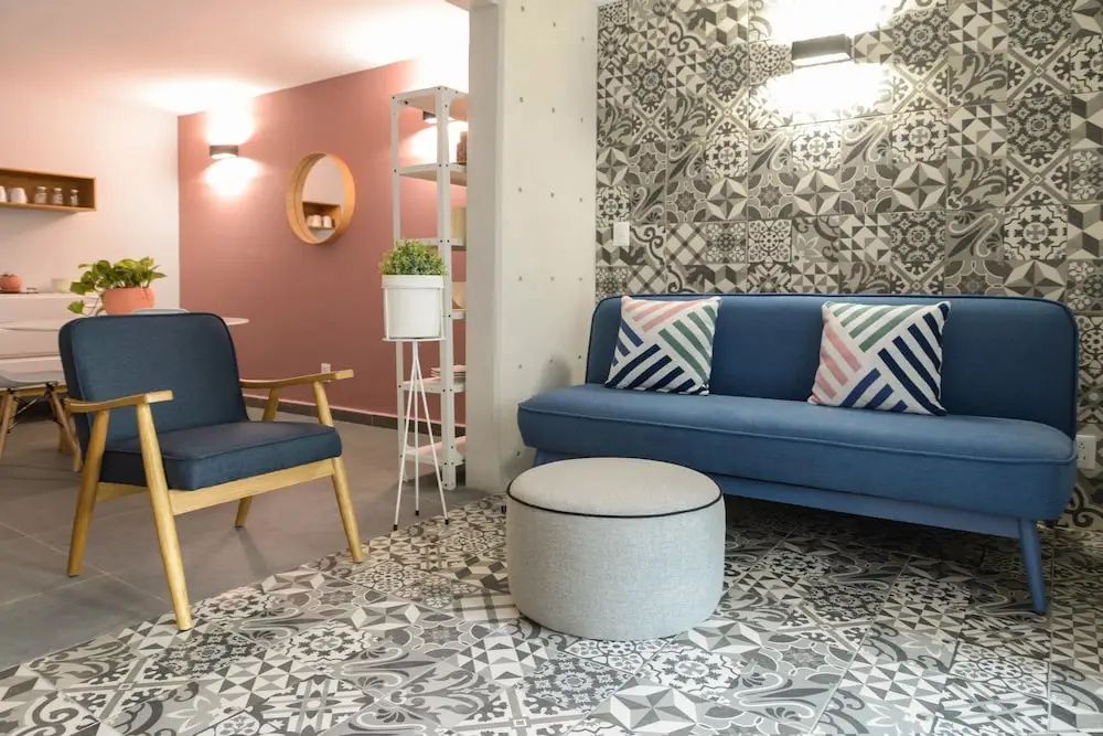 Wohnbereich mit blauem Sofa, weiß-grauem Hocker und gemustertem Fliesenboden.