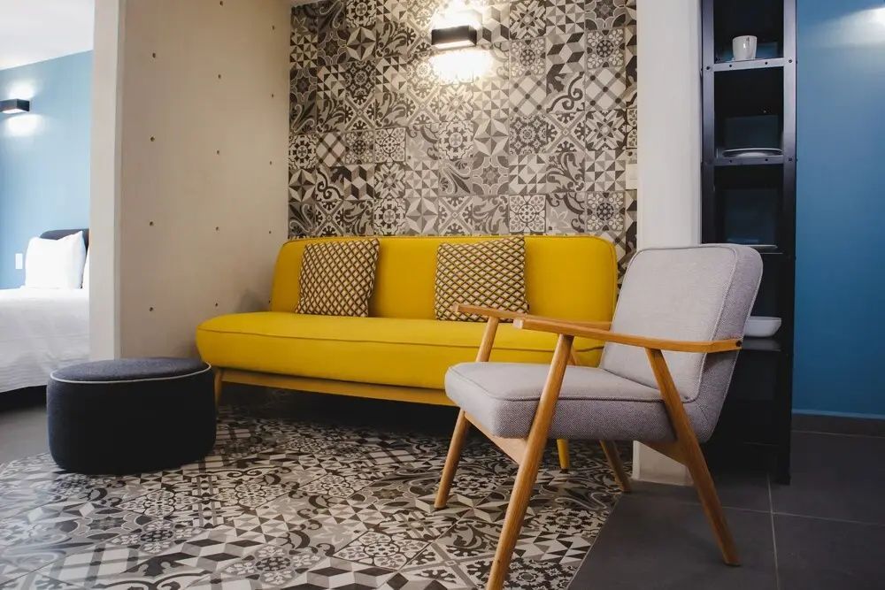 Gelbes Sofa und grauer Sessel in einer Sitzecke mit gemusterten Fliesen.
