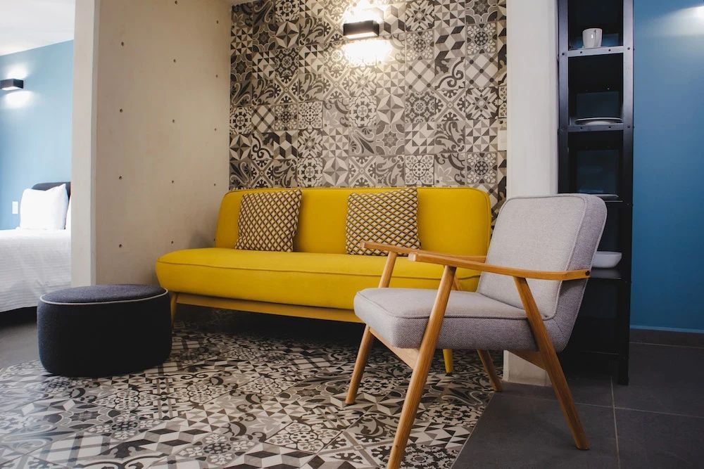 Sitzecke im Zimmer mit gelbem Sofa, grauem Sessel und gemusterten Fliesen.