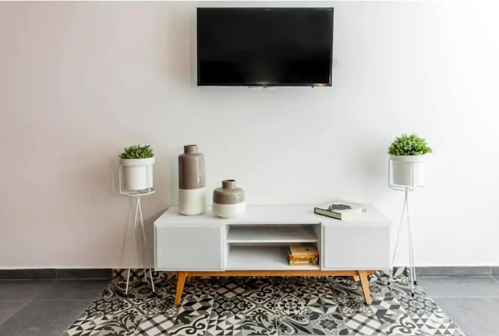 Fernseher an weißer Wand über einem weißen Lowboard auf gemustertem Fliesenboden.