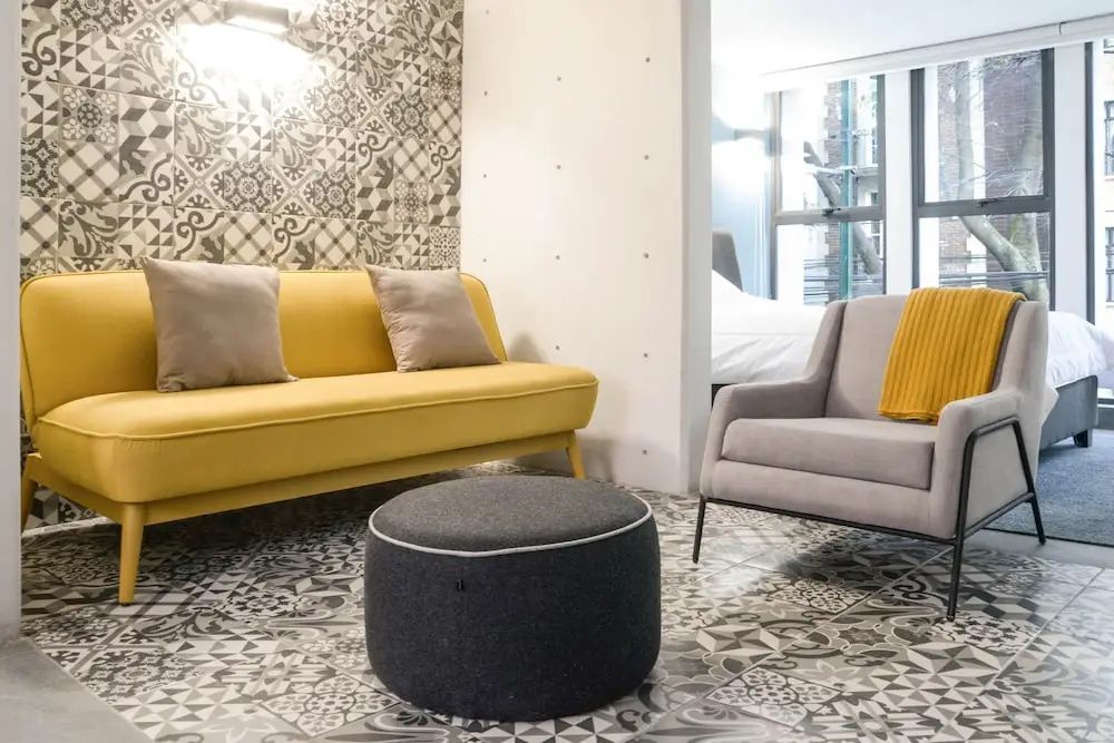 Ein gelbes Sofa und ein grauer Sessel stehen auf einem gemusterten Fliesenboden.
