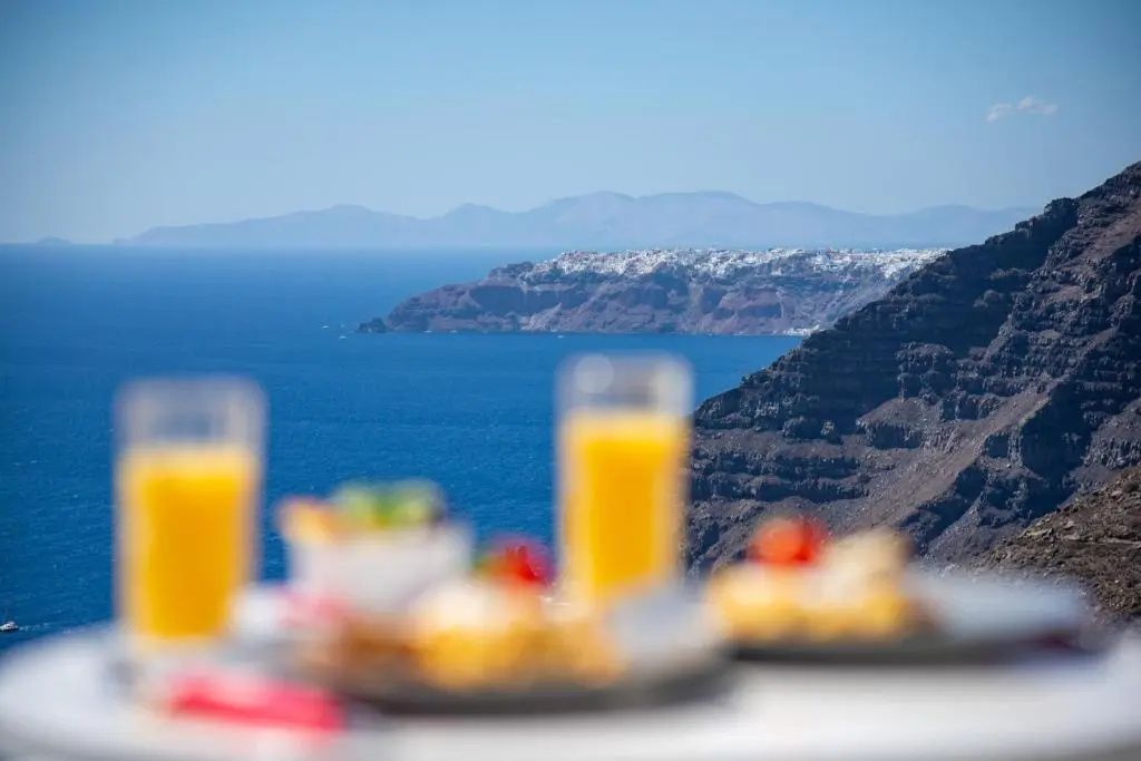 Blick über zwei Gläser Orangensaft auf das blaue Meer und die Steilküste.