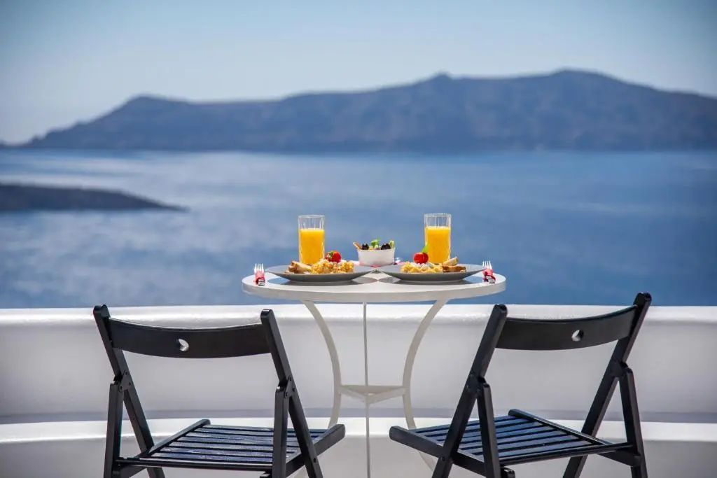 Frühstückstisch mit zwei klappbaren Stühlen auf einer Terrasse am Meer.
