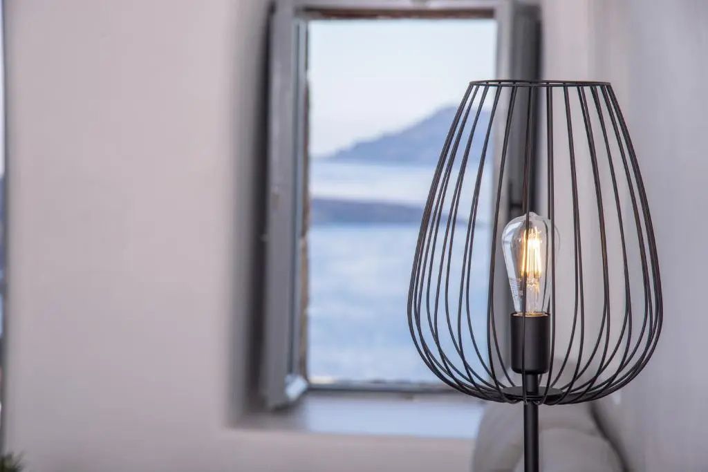 Blick durch ein geöffnetes Fenster auf das Meer hinter einer schwarzen Lampe.