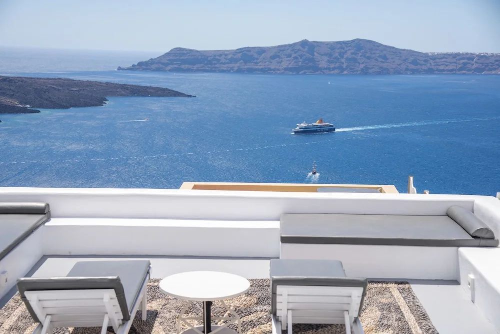 Terrasse mit zwei Sonnenliegen und freier Sicht auf das Meer und ein Schiff.