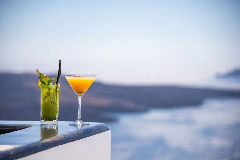 Zwei bunte Cocktails auf einer Mauer mit der blauen See im Hintergrund.