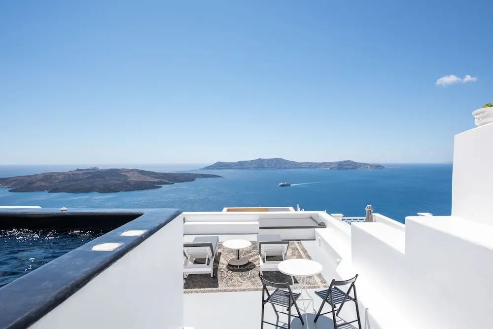 Weiße Terrasse mit Liegen und Stühlen bietet Aussicht auf die Caldera.