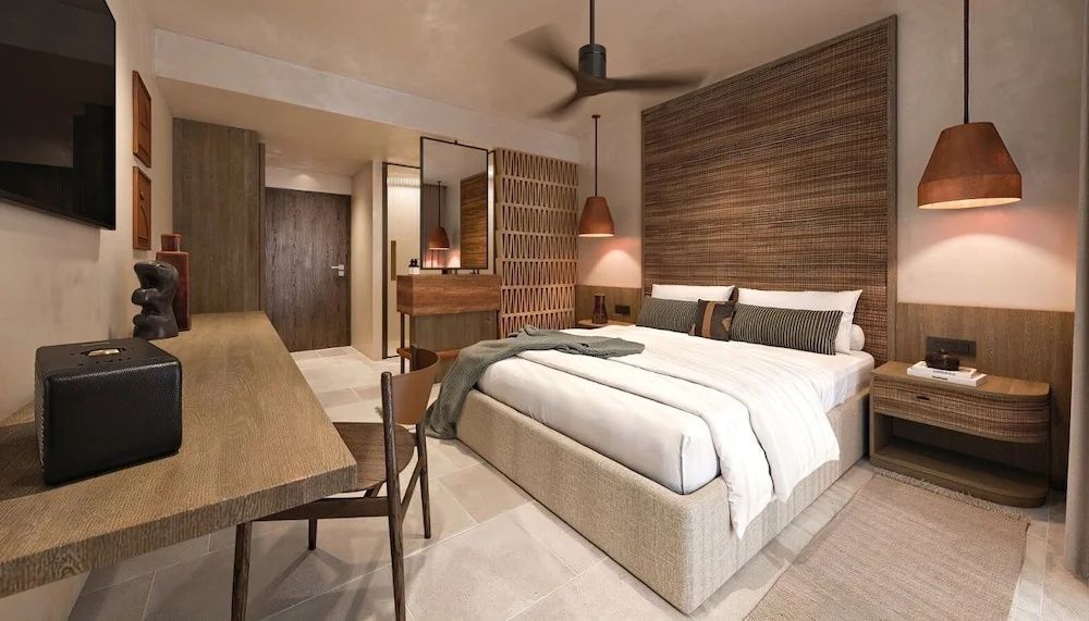 Hotelzimmer mit hellem Doppelbett, Holztisch, Stuhl und Blick in den Waschtischbereich.