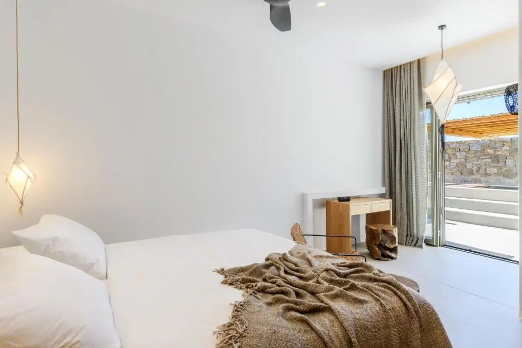 Schlafzimmer mit Doppelbett, beigefarbener Tagesdecke, Holzschreibtisch und Vorhängen.