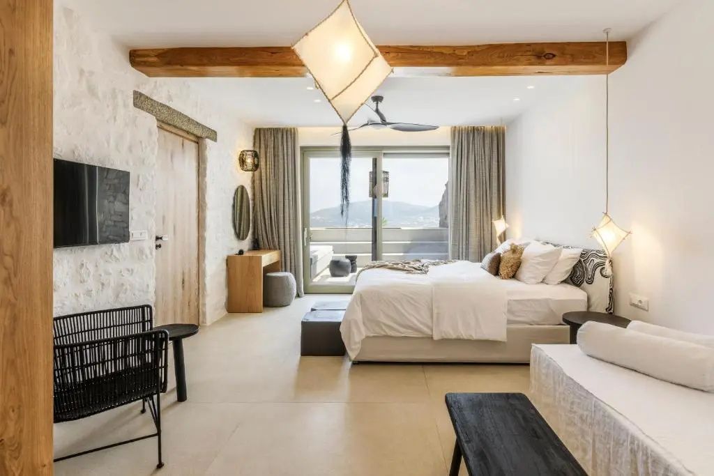 Schlafzimmer mit Doppelbett, hellem Steinboden, Holzbalken und Schiebetür zur Terrasse.
