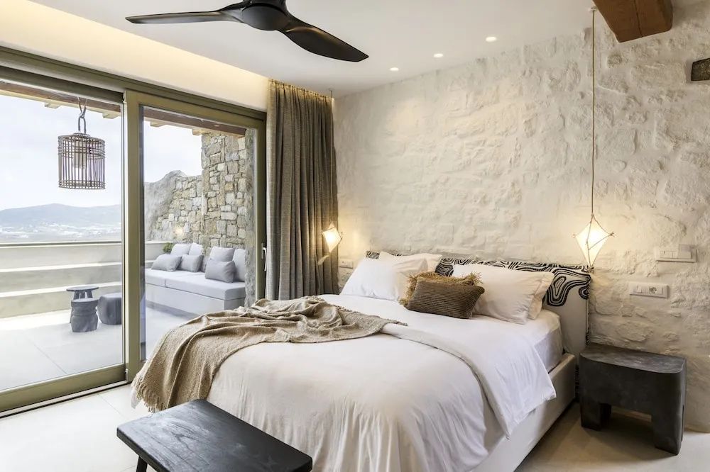 Doppelbett vor einer weißen Natursteinwand mit Blick auf die Terrasse.