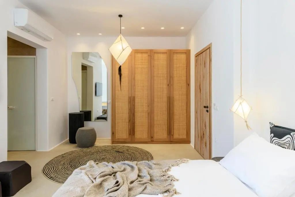 Schlafbereich mit großem Holzkleiderschrank, Wandspiegel, rundem Teppich und Hängeleuchte.
