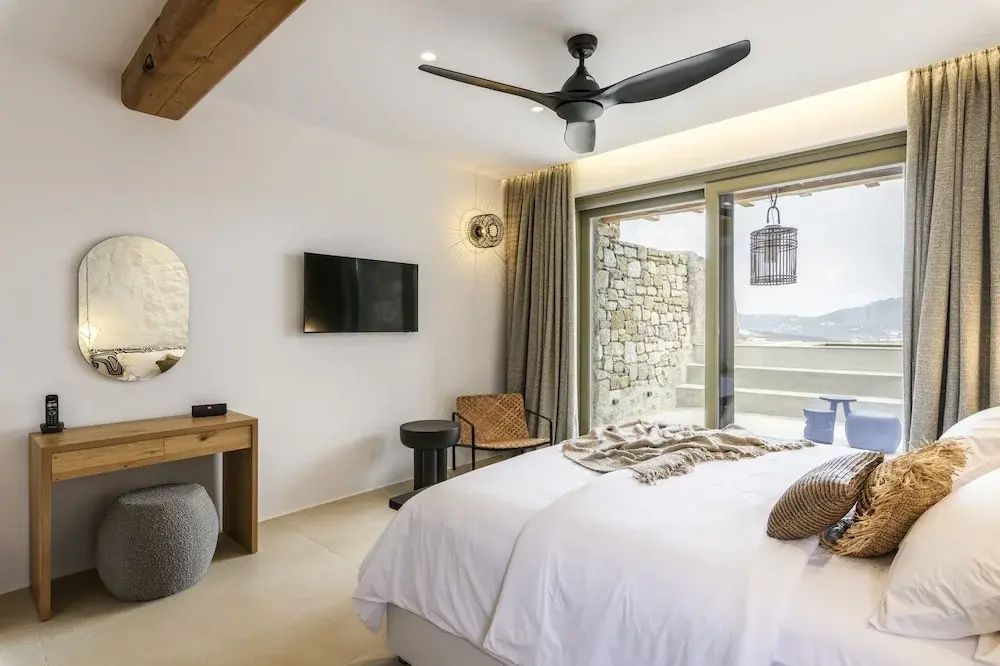 Schlafbereich mit Flachbild-TV, Schminktisch, Deckenventilator und Ausgang nach draußen.