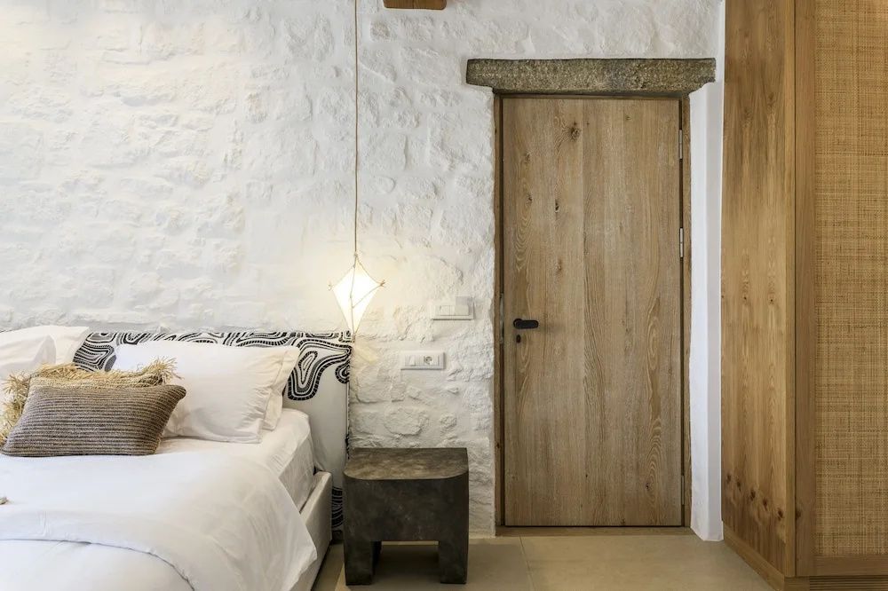 Ecke eines Schlafzimmers mit Holztür, weiß gepinselter Steinwand und Nachttisch.