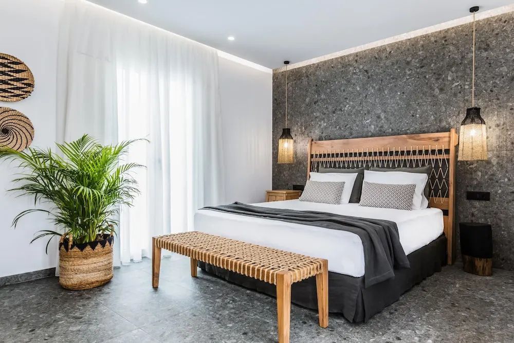 Doppelbett mit Holzkopfteil vor einer dunklen Steinwand im Hotelzimmer.