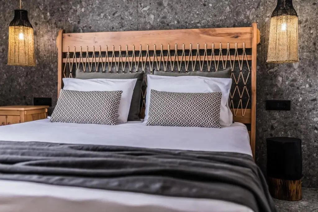 Doppelbett mit braunem Holzkopfteil, geflochtenen Seilen und grauer Tagesdecke.