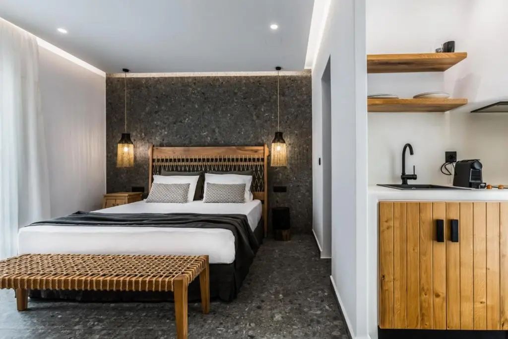 Doppelbett mit Holzkopfteil vor einer dunklen Steinwand und Hängeleuchten im Hotelzimmer.