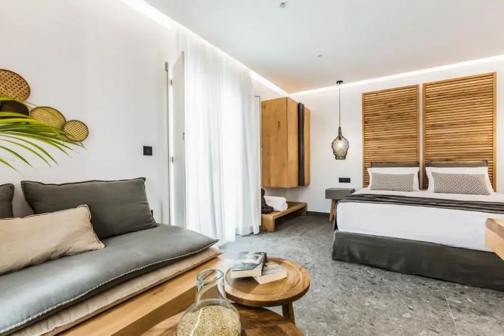 Sitzbereich im Hotelzimmer mit Holztischen und einem Doppelbett im Hintergrund.