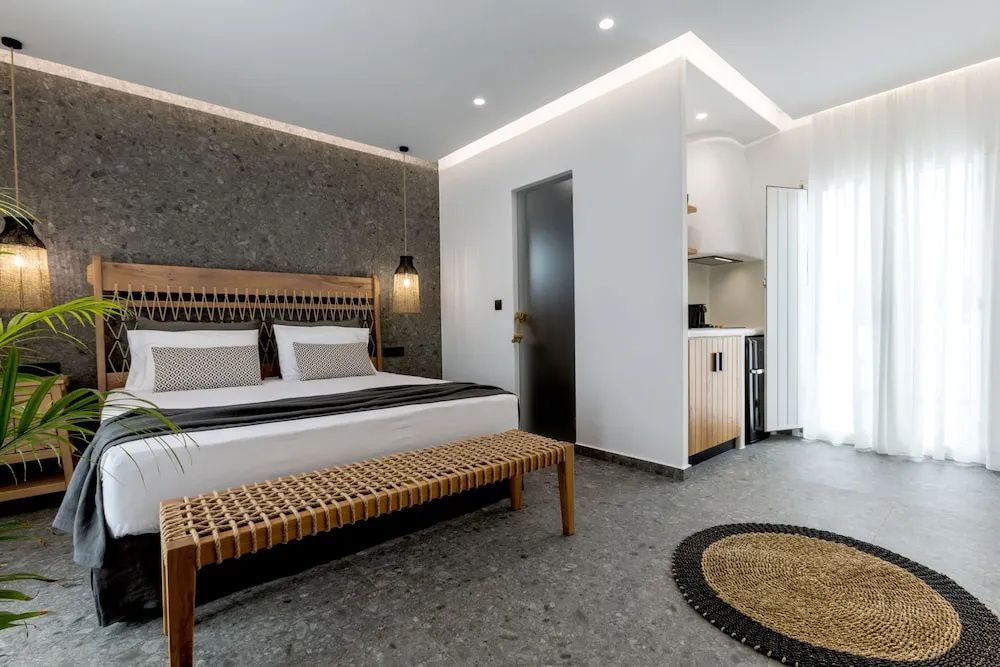 Hell eingerichtetes Schlafzimmer mit Doppelbett, Steinboden und kleiner Küchenzeile.