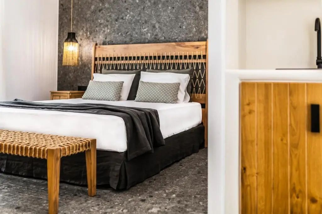 Ausschnitt eines Doppelbetts mit geflochtenem Kopfteil und Holzbank im Hotelzimmer.