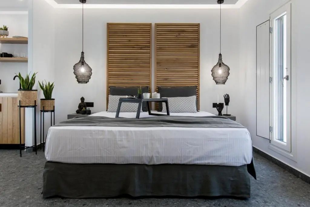 Doppelbett mit grau-weißer Bettwäsche, Holzverkleidung an der Wand und Hängeleuchten.