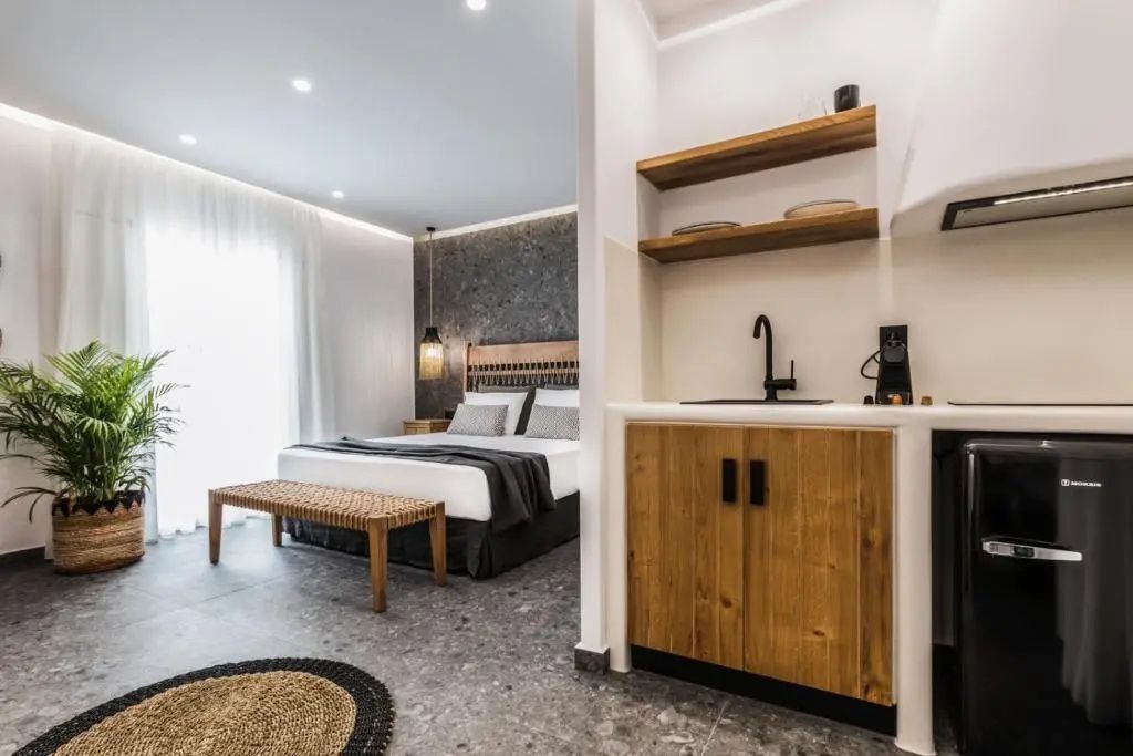 Modernes Hotelzimmer mit Doppelbett, Sitzbank und einer kleinen Küchenzeile aus Holz.
