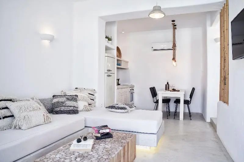 Hell eingerichteter Wohnbereich einer Suite mit weißem Sofa, Esstisch und integrierter Küchenzeile