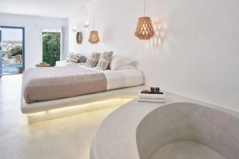 Helles Schlafzimmer mit beleuchtetem Podestbett, Holzlampen und einer integrierten Betonbadewanne.
