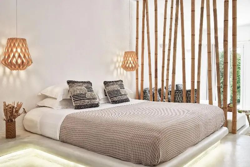 Doppelbett mit hellbrauner Tagesdecke und Kissen vor einer Trennwand aus Bambusstangen.